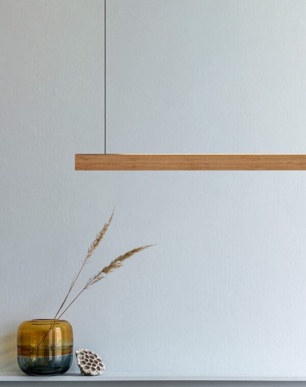 Lighture de “Massive” grijs caramel bamboe hanglamp hangend boven een vaas